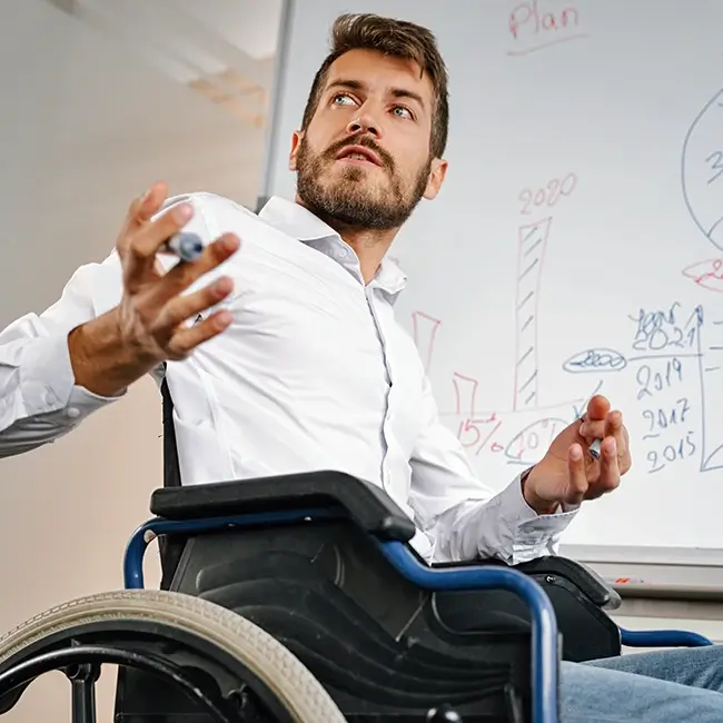 Man in wheelchair at whiteboard giving a presentation - Independent Living Movement Ireland - DPCN | Disability Participation and Consultation Network