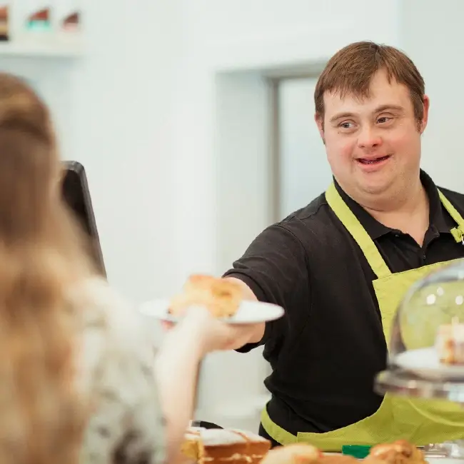 Man serving a pastry to woman - As I Am | DPCN - Disability Participation and Consultation Network