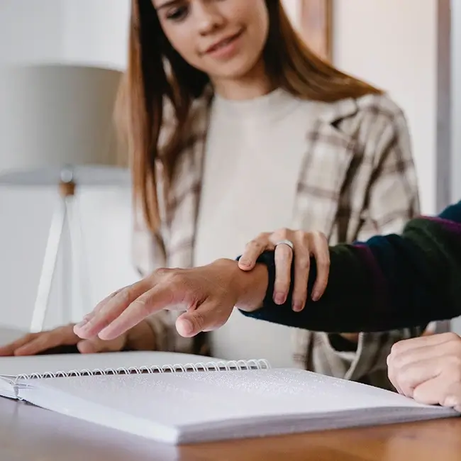 Woman guiding hand to teach braille - Disabled Women Ireland | DPCN - Disability Participation and Consultation Network